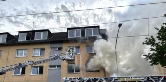 Der weiße Rauch verdeutlicht, dass bereits Löschmaßnahmen eingeleitet sind. Die Straßenbahnoberleitung erschwert den Einsatz der Drehleiter. Foto: Feuerwehr Essen/Bernd Weichert.