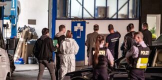 Einsatzkräfte der Polizei stehen mit weiteren Personen vor einer Autowerkstatt. Foto: Markus Klümper/Sauerland Reporter/dpa/Archivbild