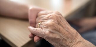 Eine Pflegerin hält die Hand einer alten Frau in einem Altenheim. Foto: Federico Gambarini/dpa/Archivbild