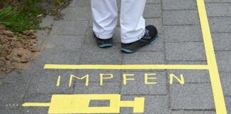 Ein Mann steht an einem Covid-19-Impfcenter hinter der Bodenaufschrift "Impfen". Foto: Arne Dedert/dpa/POOL/dpa/Symbolbild