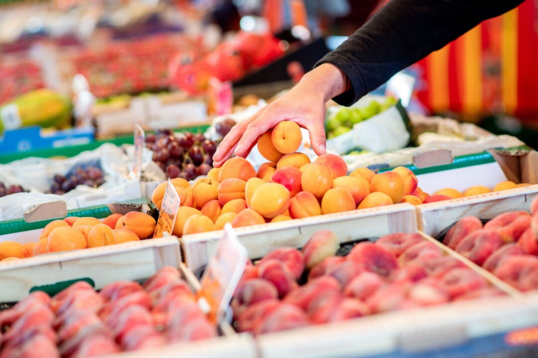 Wochenmarkt Ein Verkäufer greift an einem Obst- und Gemüsestand in eine Kiste mit Aprikosen.