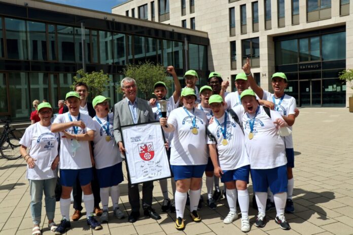 Bürgermeister Klaus Pesch und Sportdezernent Patrick Anders (3.v.l.) ehrten die erfolgreiche Fußballmannschaft der BSG Ratingen vor dem Rathaus. Als Dank für die städtische Unterstützung überreichte die BSG dem Bürgermeister ein gerahmtes Trikot mit den Namen der Teammitglieder. Foto: Stadt Ratingen