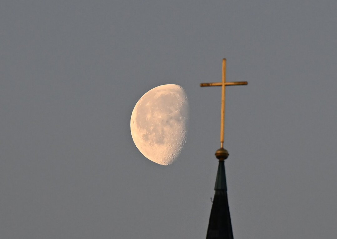 Kreuz eines Kirchturms Der Mond steht im Morgenlicht hinter einem Kreuz auf einem Kirchturm.