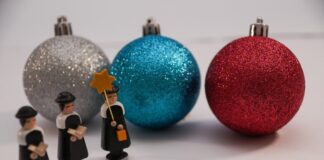 Weihnachtskugeln liegen hinter kleinen Holzfiguren auf einem Tisch. Foto: pixabay