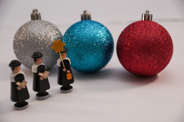 Weihnachtskugeln liegen hinter kleinen Holzfiguren auf einem Tisch. Foto: pixabay