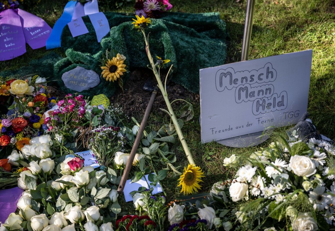 Ein Plakat mit der Aufschrift «Mensch, Mann, Held» liegt neben Blumen am Urnengrab von Malte C..