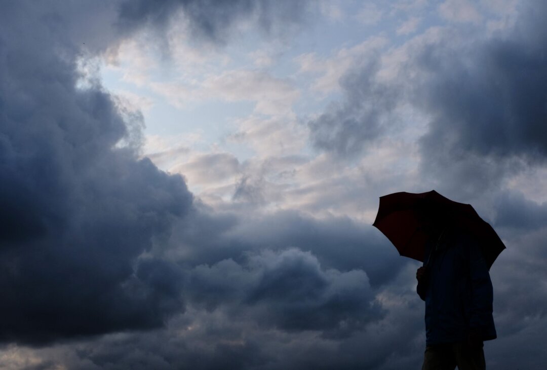Ein Mann geht mit einem Regenschirm vor aufziehenden, dunklen Wolken spazieren.
