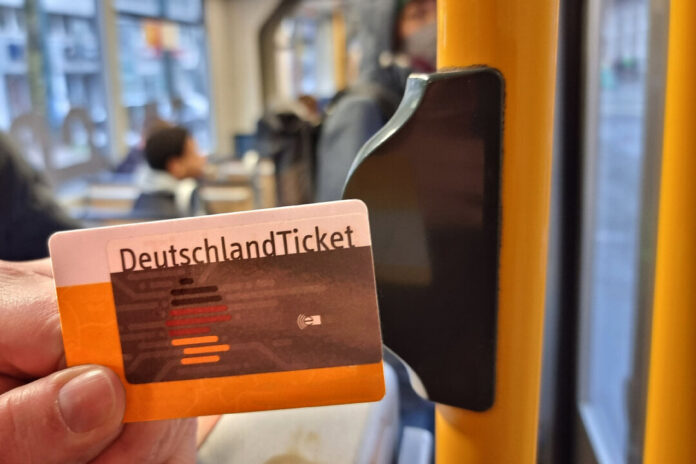 Ein Deutschlandticket wird neben eine Haltestange an der Tür einer Straßenbahn gehalten. Foto: VZ NRW