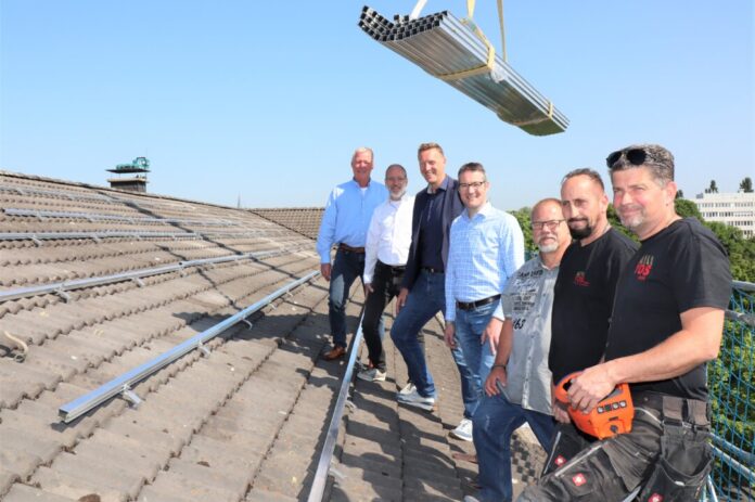 Freuen sich über den Baubeginn auf dem Dach des technischen Rathauses: Stefan Elias, Leiter des Amtes für Gebäudemanagement, Marcel Kürten, Sachgebietsleiter TGA (Technische Gebäudeausrüstung), Beigeordneter Martin Gentzsch, Peter Podgorny, Geschäftsführer der Planungsfirma ITS, Bernd Füllgräbe, Projektleiter der ausführenden Elektro-Firma des-tec sowie die Dachdecker von der Firma YOS. Foto: Stadt Ratingen