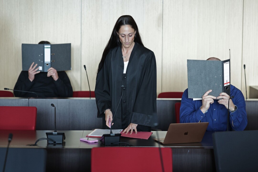 Rechtsanwältin Denise Sondermann zwischen zwei Angeklagten, die ihre Gesichter mit Aktenordnern verdecken.