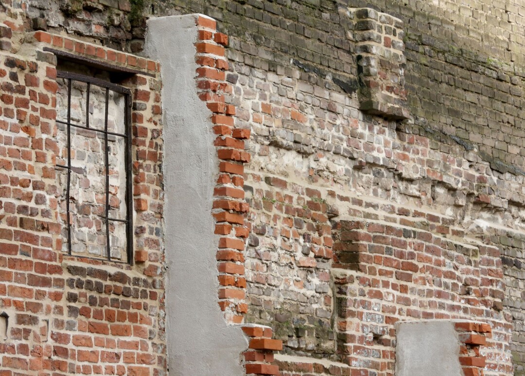 Alte Mauer mit verwittertem Fenster und Ziegeln.