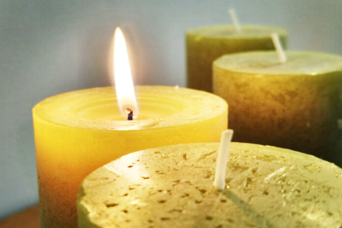 Brennende Kerze mit unangezündeten Kerzen im Hintergrund.