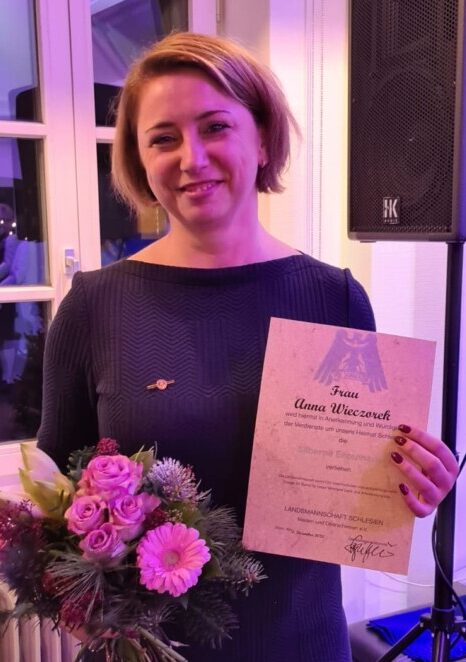 Frau mit Urkunde und Blumenstrauß lächelt.