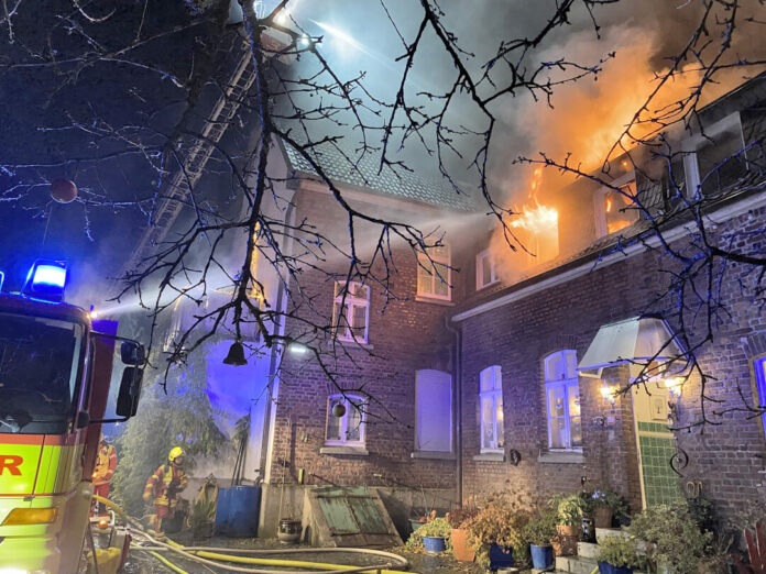 Feuerwehr löscht brennendes Haus bei Nacht.