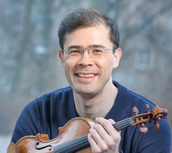 Lächelnder Geiger hält Violine im Freien.