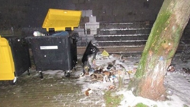 Müllcontainer bei Nacht mit verstreutem Abfall und Schnee.