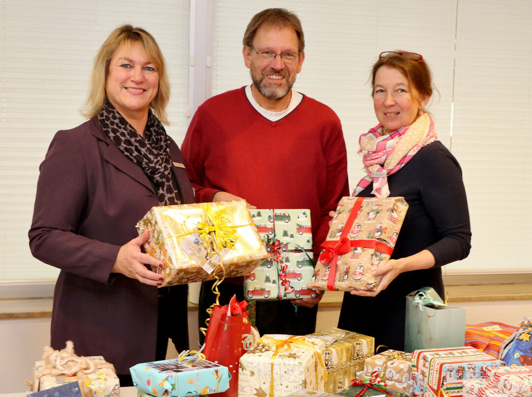 Drei Personen mit Weihnachtsgeschenken lächeln in die Kamera.