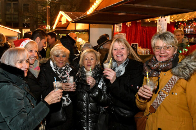 Fröhliche Gruppe genießt Weihnachtsmarktgetränke.