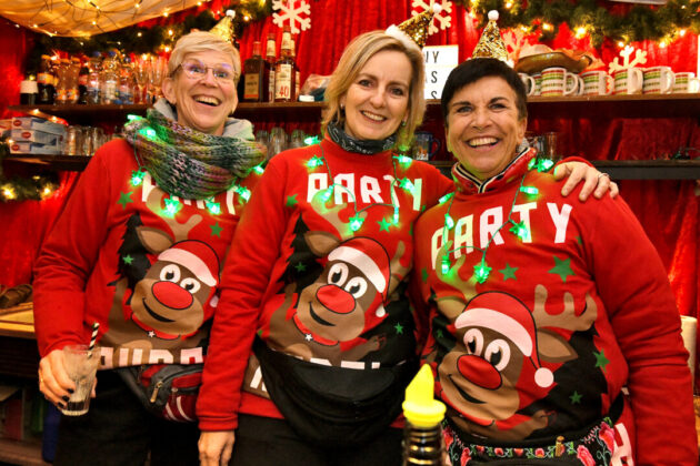 Drei Personen in lustigen Weihnachtspullovern feiern.