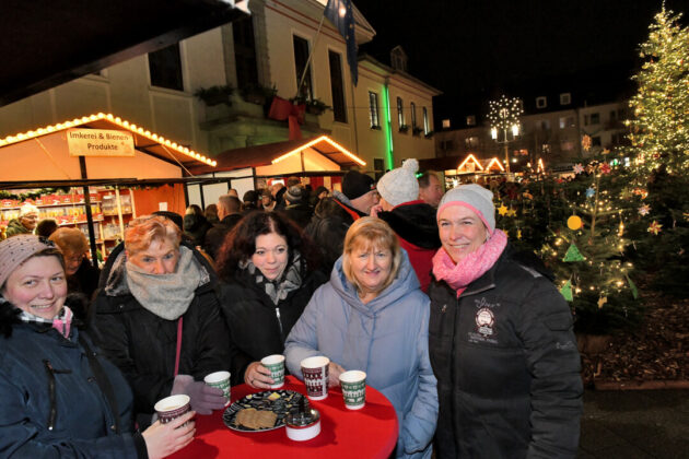 Menschen genießen deutschen Weihnachtsmarkt bei Nacht.