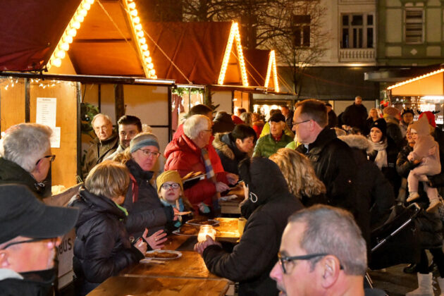 Menschen auf einem belebten Weihnachtsmarkt bei Nacht.