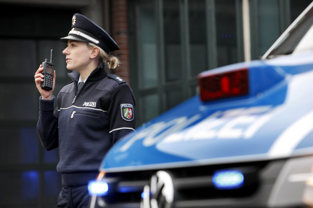 Polizistin mit Funkgerät neben Streifenwagen.