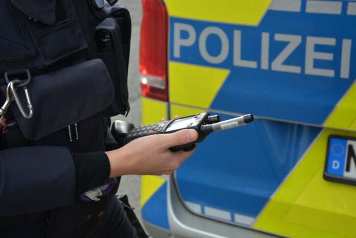 Polizist mit Funkgerät vor Polizeiauto.