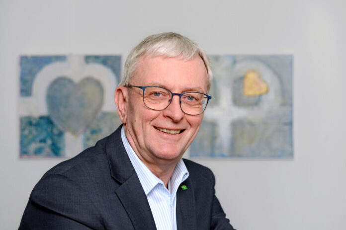 Lächelnder älterer Herr mit Brille, Anzug und Gemälde.