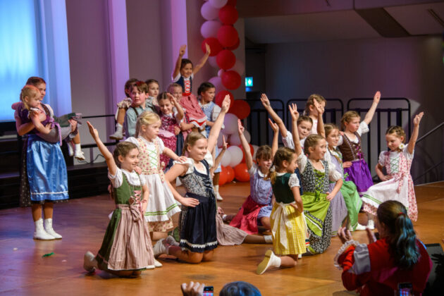 Kinder tanzen in traditioneller Tracht auf Bühne.
