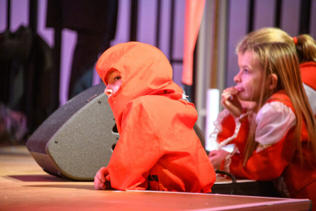 Kind in orangem Kostüm bei Aufführung.