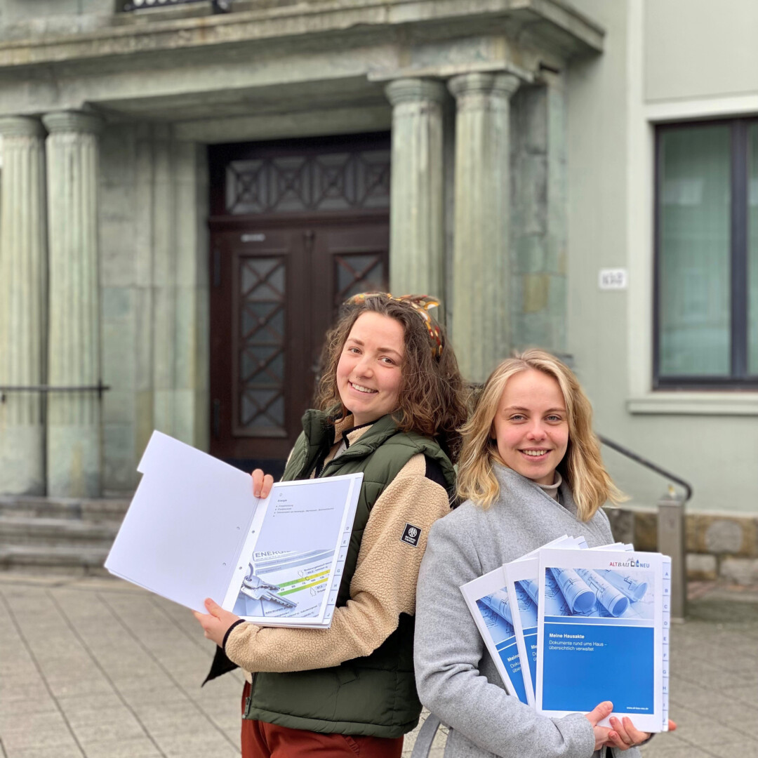 Zwei Frauen halten Unterlagen vor Gebäude.