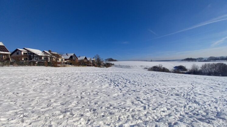 Verschneite Landschaft mit Häusern unter blauem Himmel