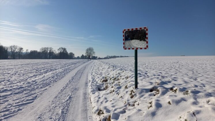 Verschneites Feld mit Verkehrsspiegel und Weg.