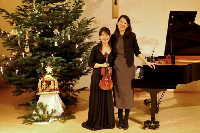 Geigerin und Pianistin neben Weihnachtsbaum und Flügel.