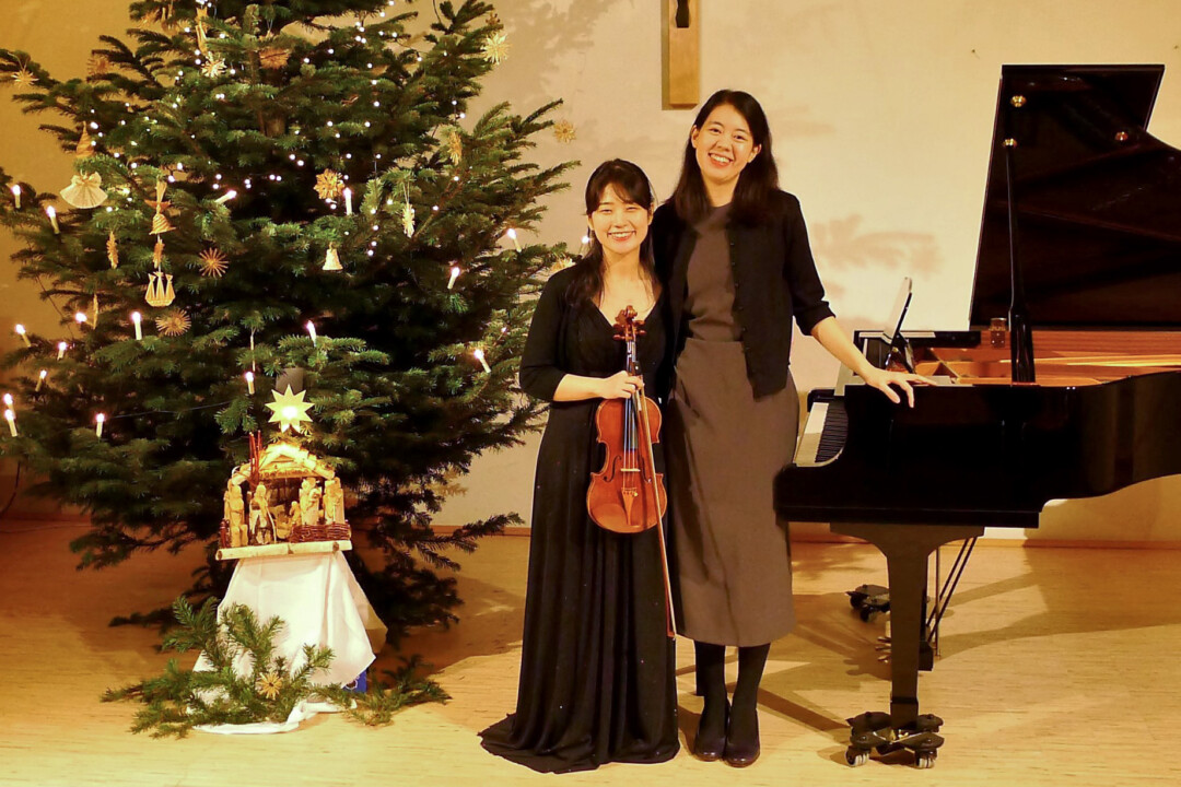 Geigerin und Pianistin neben Weihnachtsbaum und Flügel.