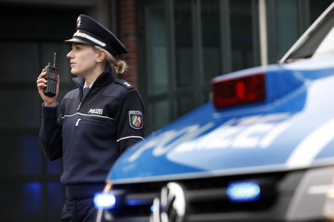 Polizistin mit Funkgerät neben Streifenwagen