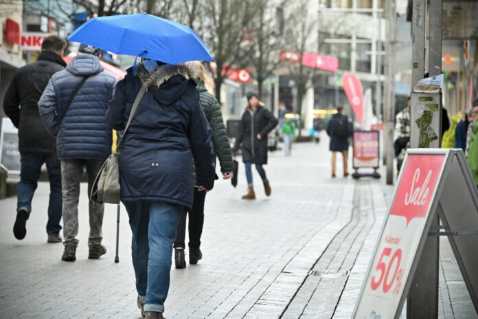 Person mit blauem Regenschirm in Einkaufsstraße.