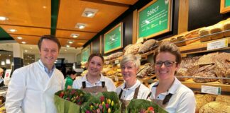 Lächelnde Mitarbeiter in Bäckerei mit Tulpensträußen.