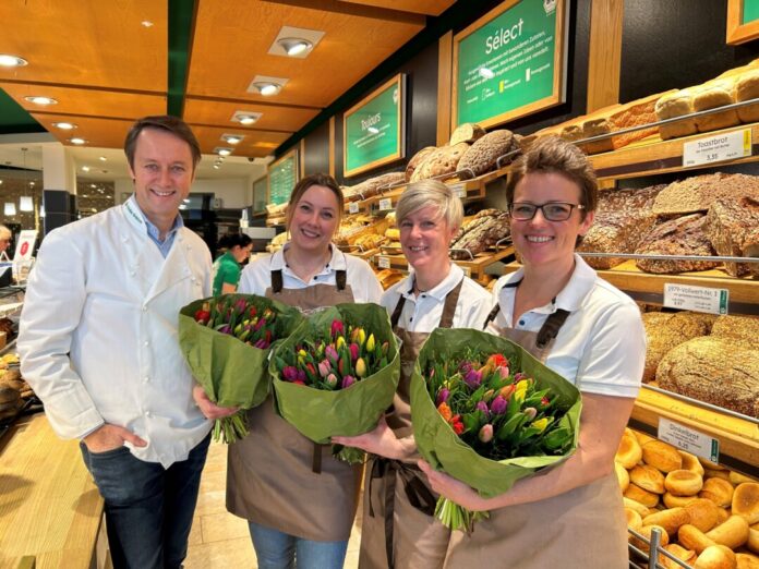 Lächelnde Mitarbeiter in Bäckerei mit Tulpensträußen.
