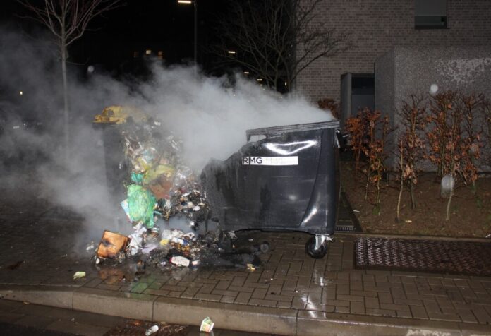 Brennender Müllcontainer mit Rauchentwicklung bei Nacht.