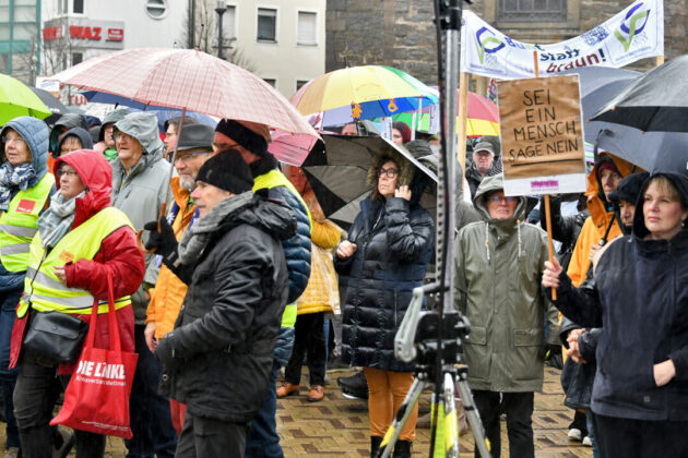 Demonstration bei Regen mit Transparenten und Regenschirmen.
