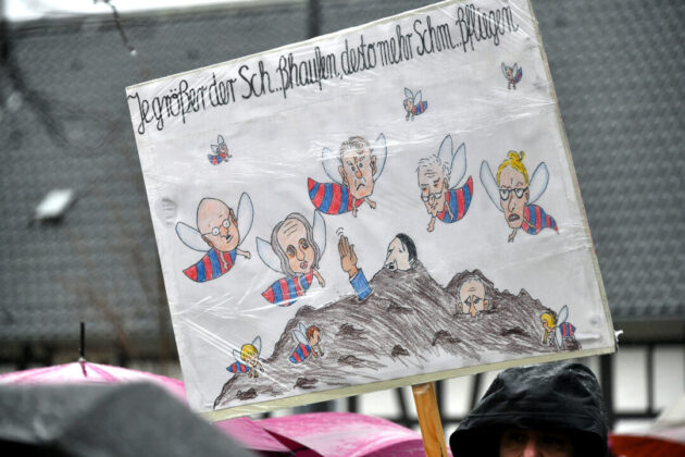 Plakat mit Karikaturen bei einer Demonstration.