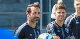 Fußballtrainer mit Ball und Spieler im Hintergrund