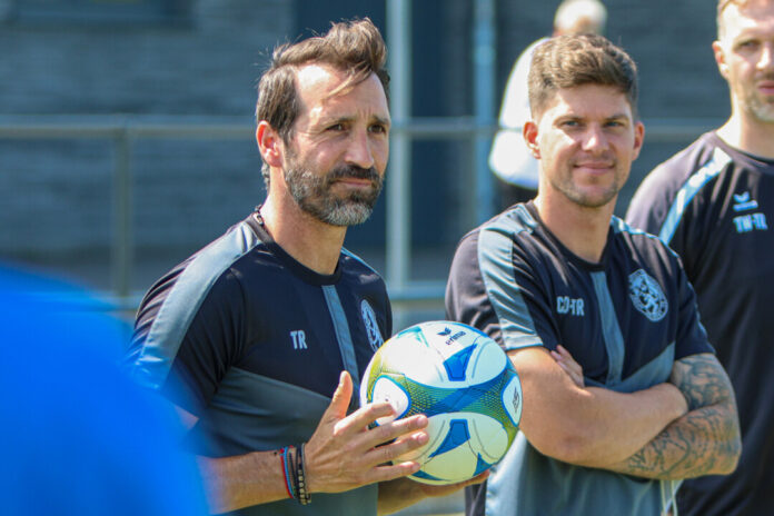 Fußballtrainer mit Ball und Spieler im Hintergrund