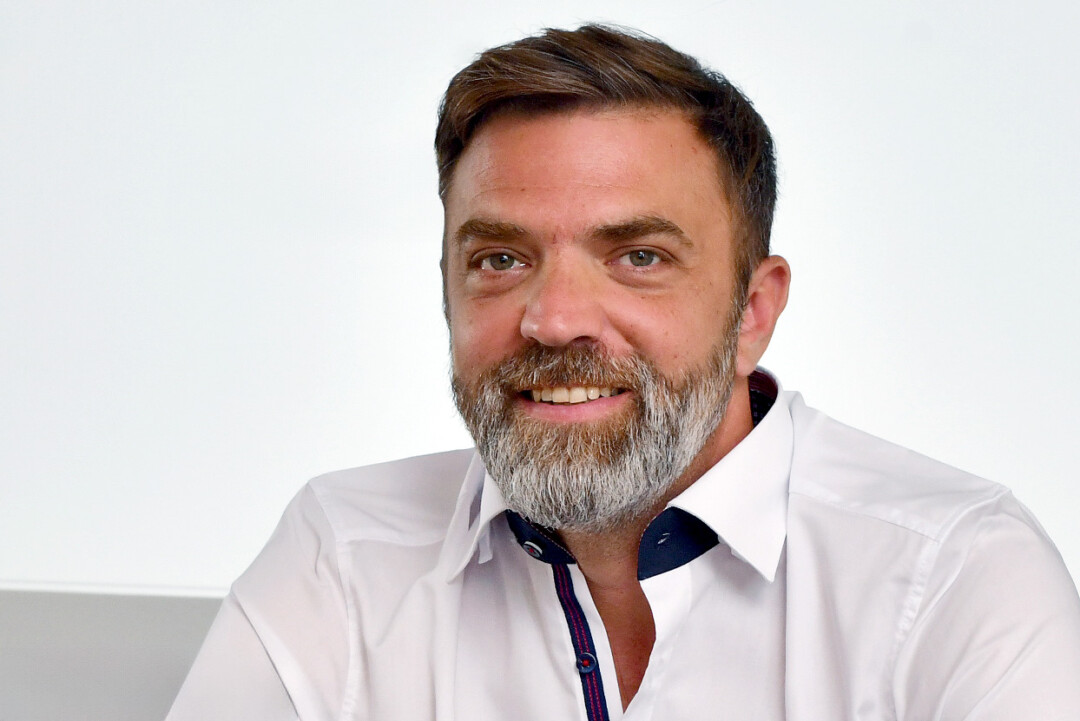 Lächelnder Mann mit Bart in weißem Hemd.