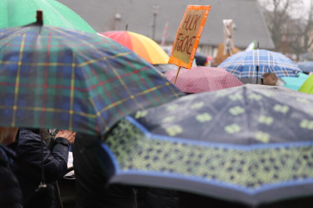Demonstration mit Regenschirmen und Protest-Schild.