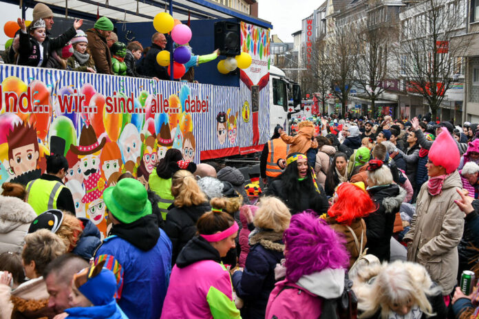 Karnevalsumzug mit Menschen und buntem Wagen.