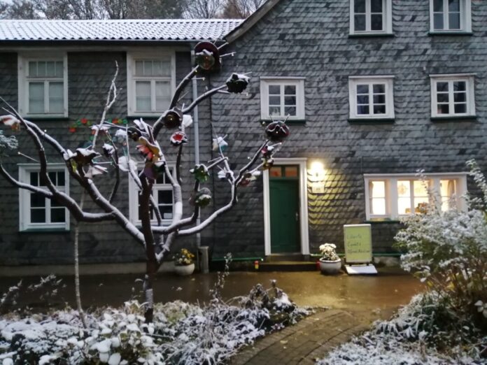 Schneebedecktes Haus mit dekoriertem Baum und Tafel.