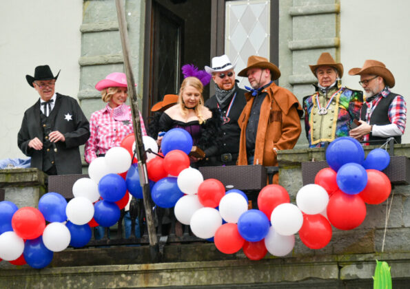 Gruppe in Kostümen mit Luftballons auf Balkon.