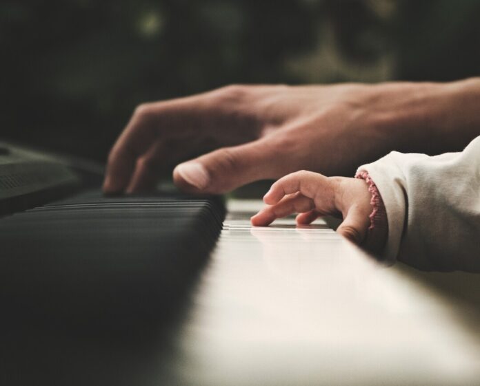 Erwachsene und Kind spielen Klavier zusammen.